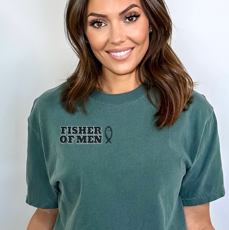 Puede incluir: Una camiseta verde oscuro con el texto "FISHER OF MEN" y un s&iacute;mbolo de pez.
