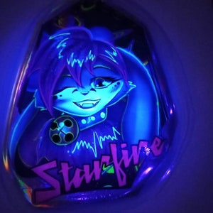 May include: A neon-lit, stylized illustration of a blue cartoon character with purple hair and a collar. The character is winking and smiling. The name "Starfire" is written in pink and green neon lettering.