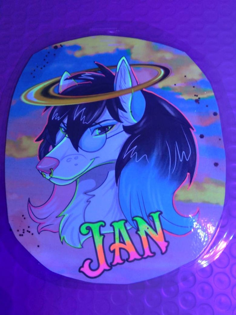 May include: A sticker featuring a stylized wolf-like character with black hair, glasses, and a halo. The character's name, "JAN," is written in vibrant green and pink letters. The background shows a colorful sky with clouds.