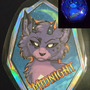 May include: A holographic sticker featuring a stylized purple wolf with horns and a stern expression. The sticker has a blue and starry background with the word "MIDNIGHT" in orange. A smaller, glowing version of the sticker is also shown.