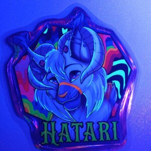 May include: A neon blue sticker with a cartoon character featuring horns and the word "HATARI" in green. The character has a light blue face with orange accents and is set against a colorful, psychedelic background.