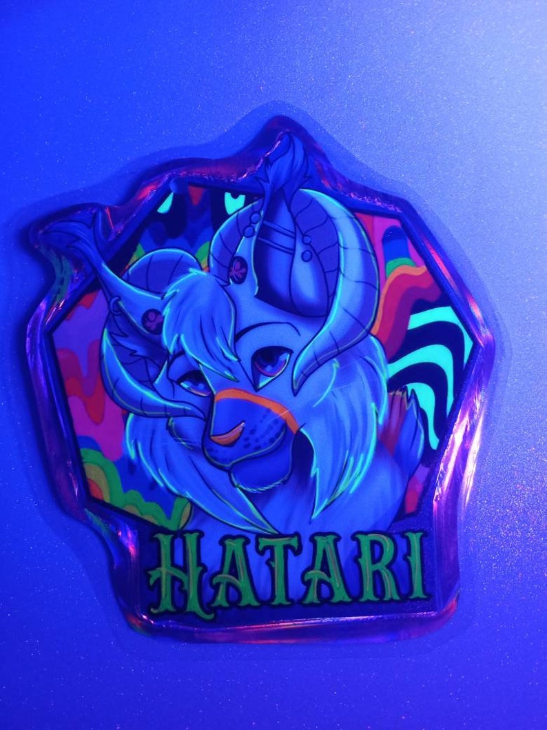 May include: A neon blue sticker with a cartoon character featuring horns and the word "HATARI" in green. The character has a light blue face with orange accents and is set against a colorful, psychedelic background.