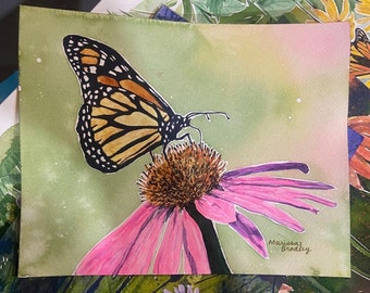 May include: Watercolor painting of a monarch butterfly with orange and black wings perched on a pink coneflower. The painting is signed "Mariposa Bradley".