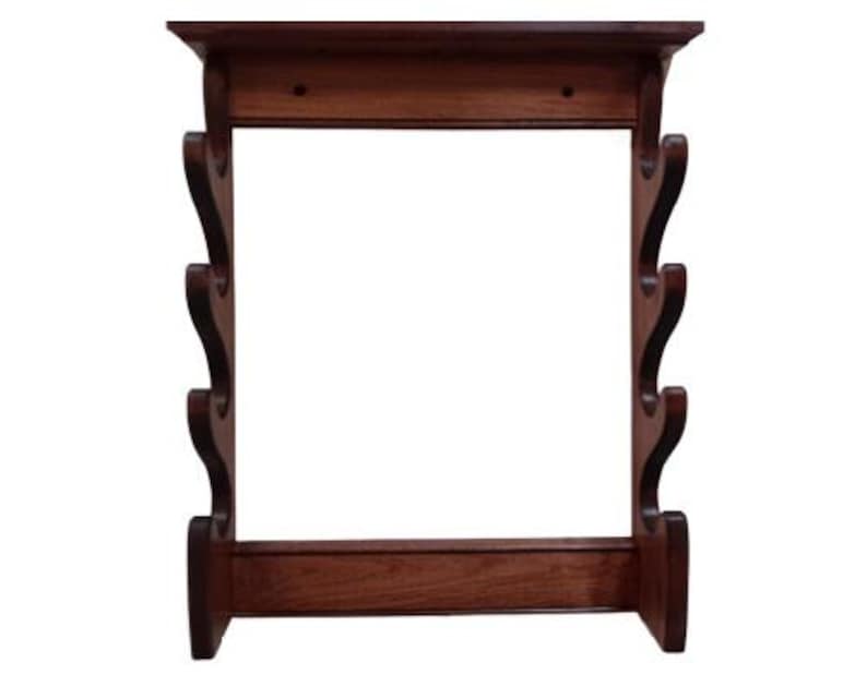 May include: A dark brown wooden wall-mounted gun rack. The rack features a top shelf, a base, and decorative curved supports. The wood has a rich, warm tone, and the design is traditional. The rack is designed to hold multiple firearms.