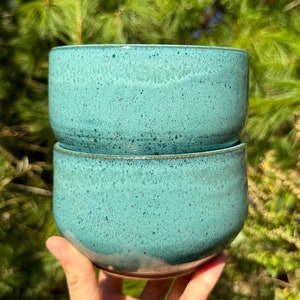 May include: Two teal ceramic bowls stacked on top of each other. The bowls have a speckled glaze and a slightly rounded shape.