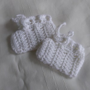 Può includere: Un paio di scarpine per neonati in crochet bianco con un fiocco su una scarpina.