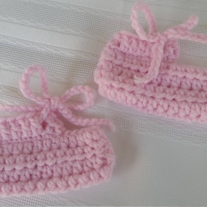 May include: Two pairs of pink crocheted baby booties with white ties.