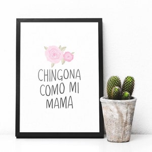 Op de afbeelding: Een zwart ingelijst afdruk met een witte achtergrond en roze bloemen. De tekst op de afdruk luidt "Chingona como mi mama".