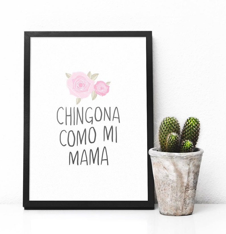 Op de afbeelding: Een zwart ingelijst afdruk met een witte achtergrond en roze bloemen. De tekst op de afdruk luidt "Chingona como mi mama".