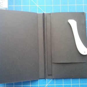 May include: A black notebook with a white plastic tool on the right side. The notebook has a spine and is closed.