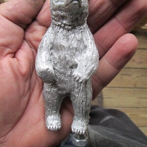 May include: A silver metal bear figurine standing on a metal base. The bear is standing on its hind legs with its paws raised. The bear has a detailed, textured surface.