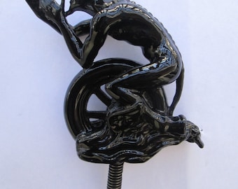 May include: Black metal figurine of a devil sitting on a wheel. The figurine is in a praying position with its hands clasped together. The figurine is mounted on a screw.