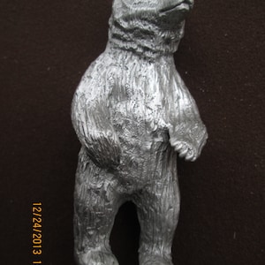 May include: A silver bear figurine standing on a metal base. The bear is standing on its hind legs with its paws raised. The bear has a detailed, textured surface.