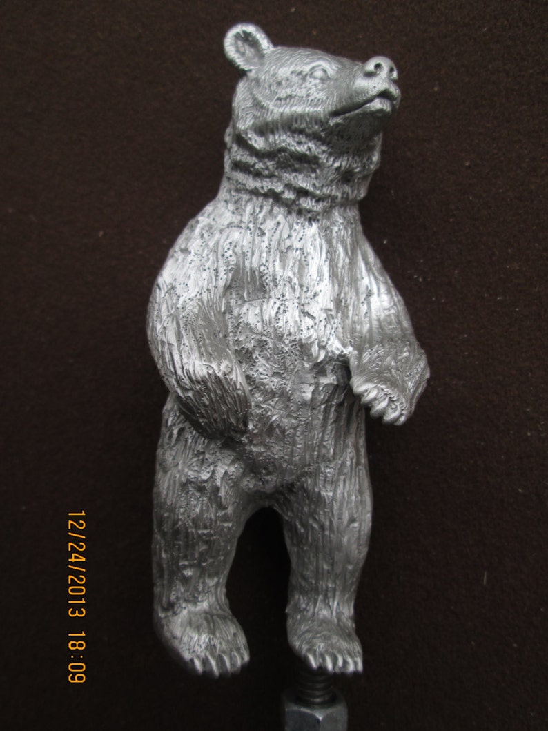 May include: A silver bear figurine standing on a metal base. The bear is standing on its hind legs with its paws raised. The bear has a detailed, textured surface.