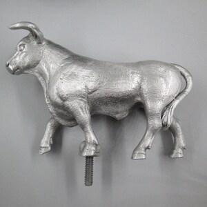 May include: A silver metal bull figurine with a textured surface. The bull is standing on a screw-like base.