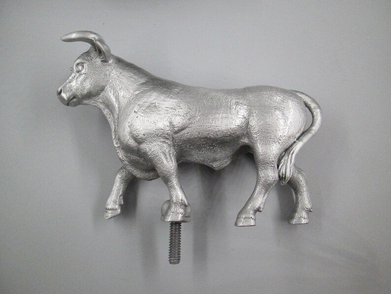 May include: A silver metal bull figurine with a textured surface. The bull is standing on a screw-like base.