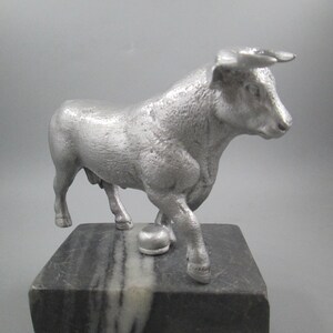 May include: A silver metal sculpture of a bull standing on a black and white marble base.