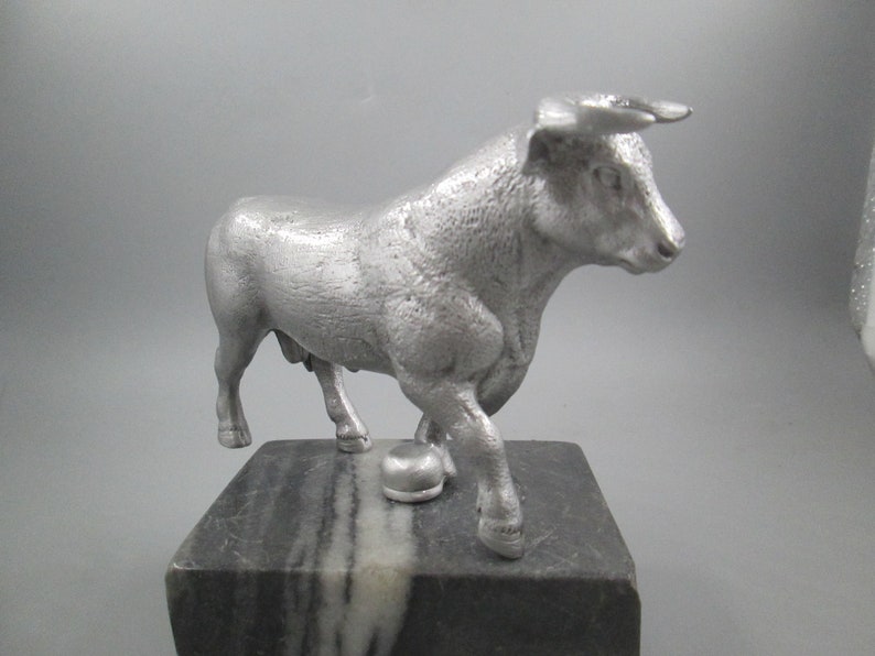 May include: A silver metal sculpture of a bull standing on a black and white marble base.
