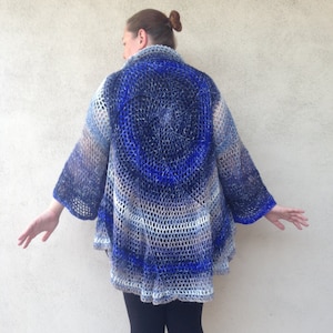 May include: A blue and white crocheted cardigan with a circular design on the back. The cardigan is open in the front and has long sleeves.
