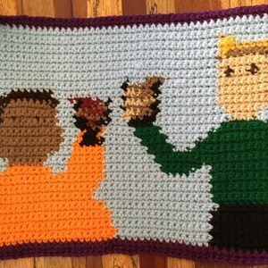 May include: Crocheted artwork featuring two people with different skin tones. The person on the left is wearing orange and the person on the right is wearing green. The background is light blue.