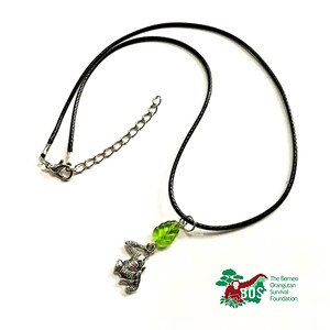 May include: A black cord necklace with a silver orangutan charm and a green glass leaf pendant. The Borneo Orangutan Survival Foundation logo is in the bottom right corner.