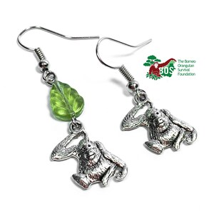 May include: Silver orangutan earrings with a green leaf charm. The earrings are made by the Borneo Orangutan Survival Foundation.