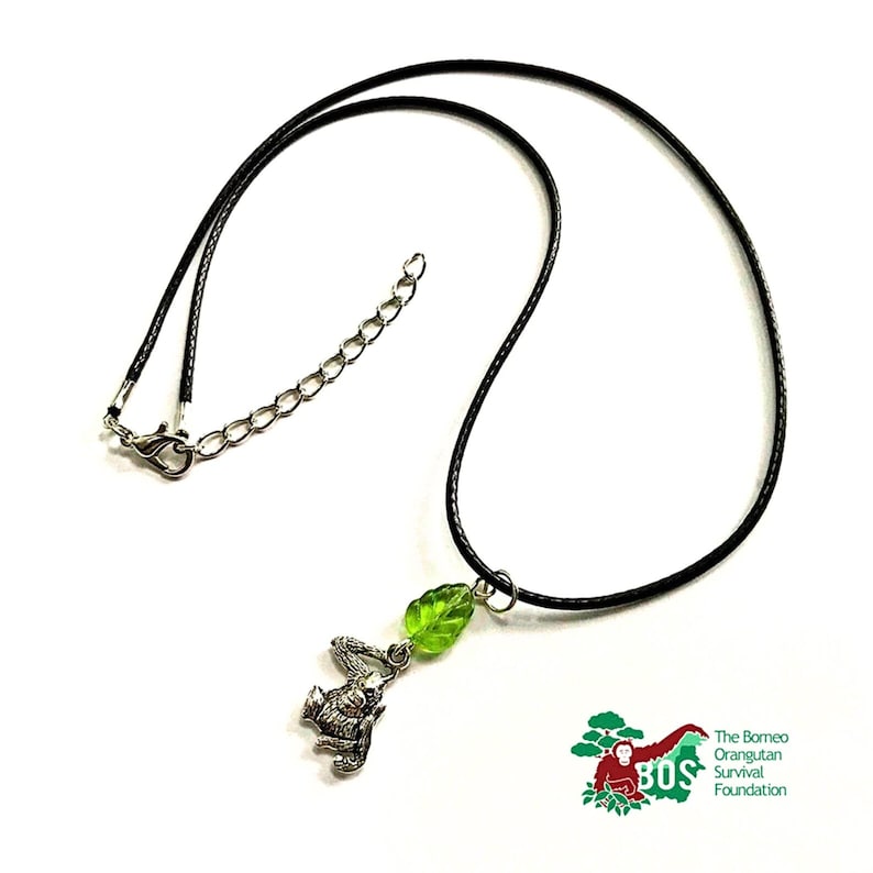 May include: A black cord necklace with a silver orangutan charm and a green glass leaf pendant. The Borneo Orangutan Survival Foundation logo is visible in the bottom right corner.