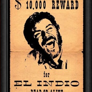 May include: A framed poster featuring a tan, aged-paper background with black text and a central black-and-white illustration of a laughing man. The text reads $ 10,000 REWARD for EL INDIO DEAD OR ALIVE, presented in a bold, western-style font.