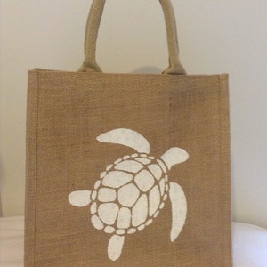 May include: A brown burlap tote bag with a white sea turtle design. The bag has a single handle.