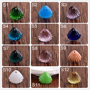 May include: Twelve different colored glass seashell charms with a hole at the top for stringing. The charms are arranged in a grid pattern on a wooden surface.