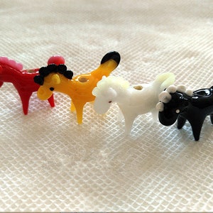 Puede incluir: Cuatro pequeñas figuritas de caballo de vidrio en rojo, amarillo, blanco y negro.