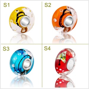 May include: Four glass beads with silver-colored metal cores. Each bead has a unique design: yellow with black, orange with black, blue with black, and red with white polka dots and a floral design. The beads are transparent.