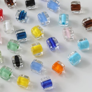 May include: Assortment of colorful glass beads in various colors, including blue, green, yellow, orange, red, pink, and brown. The beads are square shaped and have a translucent appearance.