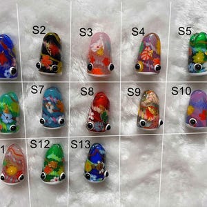 May include: Thirteen colourful, hand-painted, glass figurines with whimsical faces and floral designs. Each figurine is labelled with a letter and number, from S1 to S13.