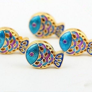May include: Four gold-coloured fish charms with blue and purple enamel detailing. The fish have a detailed scale pattern and a small blue circle for an eye.