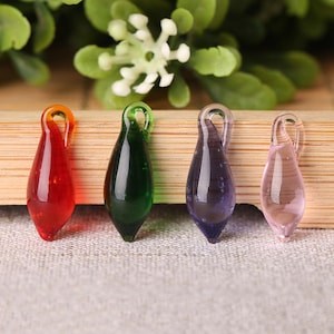 May include: Four glass teardrop-shaped charms in red, green, purple, and clear. Each charm has a small loop at the top for attaching to a necklace or bracelet.
