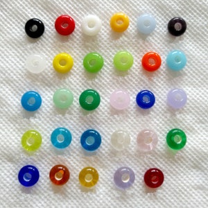 May include: Assortment of 25 round glass beads in various colors, including black, red, white, yellow, green, blue, and purple. The beads have a hole in the center for stringing.