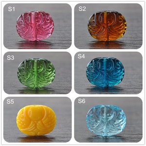 May include: Six glass beads with intricate carvings in the shape of a bird. The beads are in various colours: pink, brown, green, blue, yellow, and light blue.