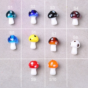 May include: Ten glass mushroom charms in various colors, including blue, red, yellow, black, white, and orange. Each charm has white stems and a different colored cap with white polka dots.