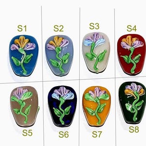 Puede incluir: Ocho cuentas de vidrio con diseños florales en varios colores, incluyendo azul, verde, rojo, amarillo, blanco y marrón. Cada cuenta está etiquetada con un número del S1 al S8.