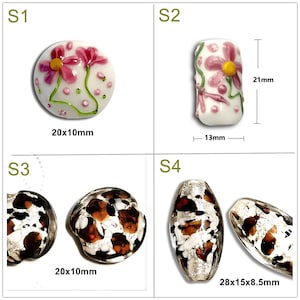 May include: Four glass beads with different designs. The first bead is white with pink flowers and green stems. The second bead is white with pink flowers and green stems. The third bead is brown with white spots. The fourth bead is brown with white spots. The beads are all different sizes.