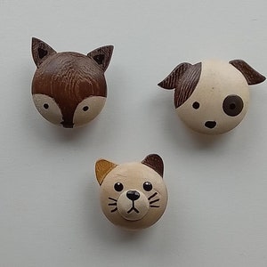May include: Three wooden animal head ornaments. A brown fox, a brown and white dog, and a brown and white cat.