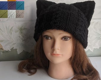 May include: Black knitted cat ear beanie hat with a cable knit pattern. The hat is worn on a mannequin head with long black hair.