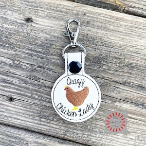May include: White round keychain with a brown chicken and the text "Crazy Chicken Lady".