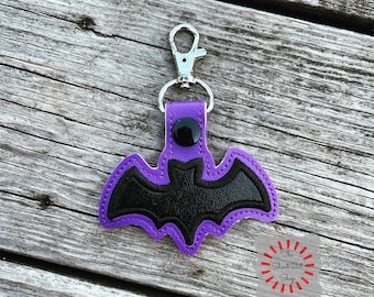 May include: Purple leather keychain with a black bat design. The keychain has a silver metal clasp.