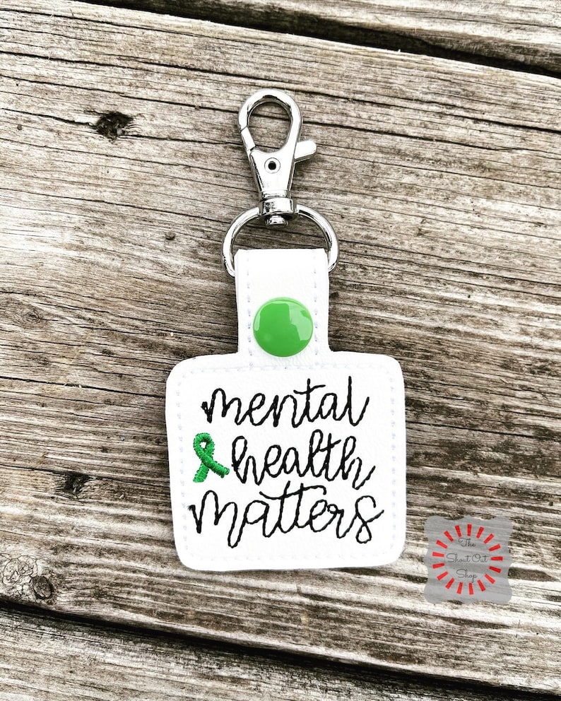 May include: White square keychain with a green ribbon and the text "mental health matters" in black cursive lettering. The keychain has a silver clip and a green button.