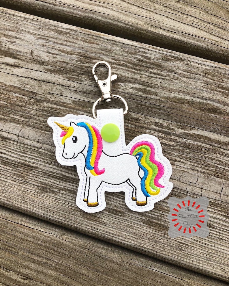 May include: A white unicorn keychain with a rainbow mane and tail. The keychain has a silver clip and a green button.
