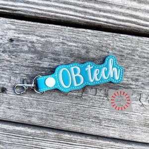 May include: A teal blue key chain with a white embroidered design that says "OB tech".