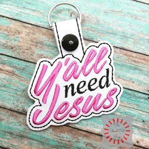 May include: White leather keychain with a pink embroidered phrase "Y'all need Jesus".