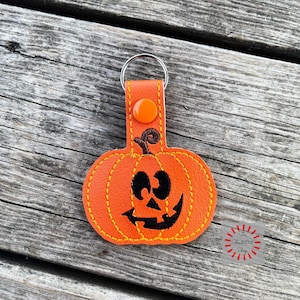 May include: Orange leather pumpkin keychain with a stitched black jack-o'-lantern face and a silver key ring.